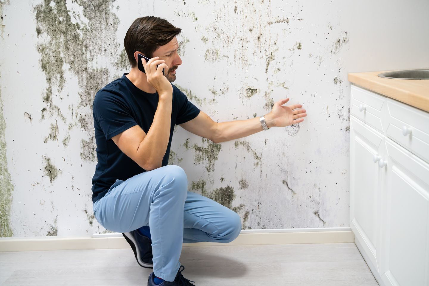 Mann telefoniert vor einer großflächig mit Schimmel befallenen Wand